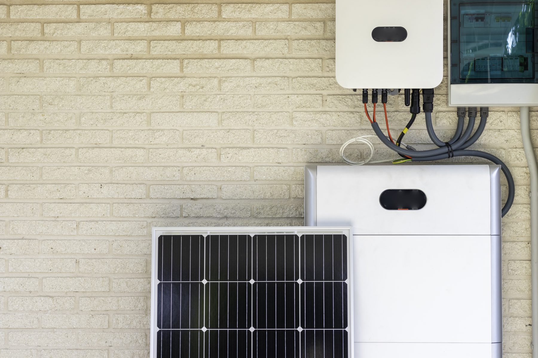 A solar panel, wall-mounted battery stack and hybrid inverter installed together on a house wall