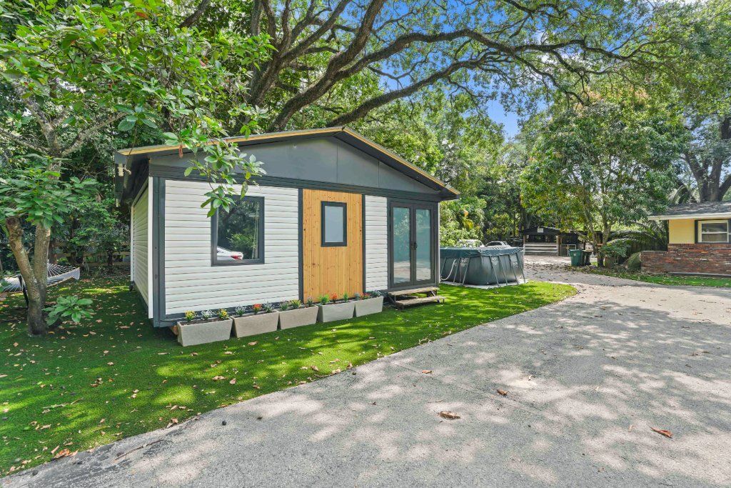 PLAD OMNI accessory dwelling unit with white siding and a wood front door beneath mature oaks